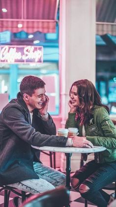 two people sitting at a table talking on their cell phones in a restaurant with neon lights behind them