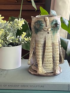 an elephant statue sitting on top of a book next to a potted plant and flowers