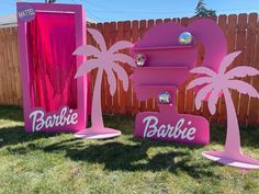 two pink signs with palm trees and the word barbie on them in front of a wooden fence