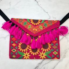 a pink purse with tassels and flowers on it sitting on a marble surface