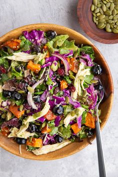 a large salad in a wooden bowl with a spoon on the side next to it