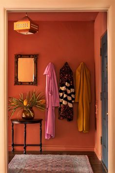 a hallway with an orange wall and coat rack on the wall, mirror above it