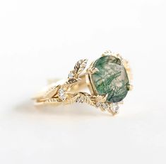 This exquisite Moss Agate ring set features the serene beauty of nature captured in elegant simplicity. Crafted with care, it showcases the captivating charm of moss agate, a stone renowned for its lush green hues and intricate patterns reminiscent of verdant forests. The delicate leaf motif adorning the band adds a touch of organic grace, enhancing the ring's natural charm. Nature-inspired Rings With May Birthstone Gemstone, Nature-inspired Gemstone Rings For May Birthstone, Nature-inspired Rings With May Birthstone, Gold Emerald Ring With Nature-inspired Design, Green Emerald Jewelry With Rose Cut Diamonds, Nature-inspired Natural Stones Jewelry For Anniversary, Nature-inspired Yellow Gold Gemstone Rings, Nature-inspired Rings With Natural Stones For Promise, Nature-inspired Natural Stones Promise Ring