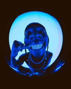 a woman is smiling and holding a toothbrush in her mouth with blue light shining on her face