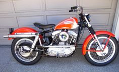 an orange and white motorcycle parked in front of a garage