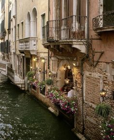 an alleyway with flowers on the windows and people sitting at tables in the water