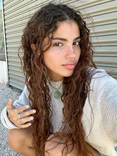 a young woman with long curly hair posing for the camera in front of a garage door