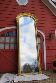 a large gold framed mirror sitting in front of a red building with a white door