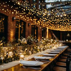 a long table is set with white plates and place settings, lit by string lights