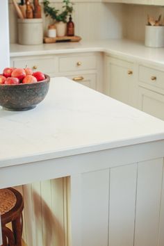 a bowl of fruit sitting on top of a white counter in a kitchen next to an oven