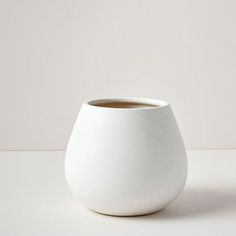 a white vase sitting on top of a table next to a cup filled with liquid