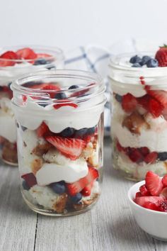 four mason jars filled with fruit and yogurt on top of a wooden table