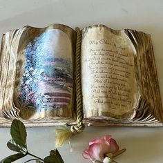 an open book sitting on top of a table next to a flower