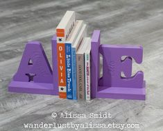 purple bookends with books stacked on top of each other in the shape of letters