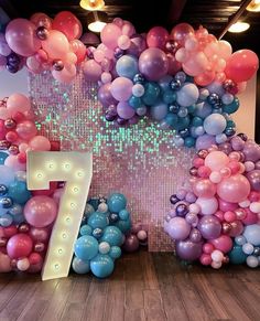 the number seven is surrounded by balloons in pink, blue and purple colors on display