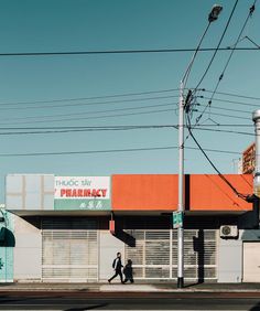 two people walking down the street in front of an empty building with orange awnings