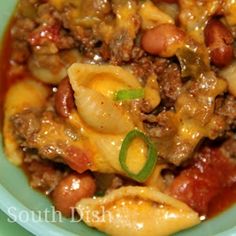 a green bowl filled with pasta and meat covered in sauce on top of a table