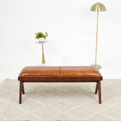 a small bench with a plant on it in front of a white wall and rug