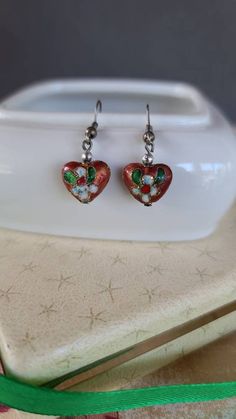 These are a very pretty pair of vintage dangling cloisonne heart shaped earrings. Unsigned. A few light surface scratches and some minor discoloration consistent with age. Please see photos. Sold as is. Priced accordingly. Will be packaged in a gift box perfect for giving. I will refund any shipping overages. Does not include any props in photos. Please feel free to contact me with any questions you may have. Before you buy, please note that the items in my shop are pre-owned and may (or may not Heart Charm Enamel Earrings, Heart-shaped Enamel Earrings With Charm, Handmade Heart-shaped Enamel Earrings, Vintage Pierced Enamel Earrings, Vintage Nickel-free Enamel Earrings, Vintage Multicolor Enamel Earrings, Vintage Drop Earrings For Valentine's Day, Vintage Heart-shaped Enamel Jewelry, Vintage Heart Charm Drop Earrings