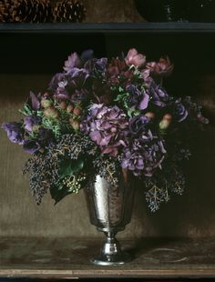 a silver vase filled with purple flowers on top of a table