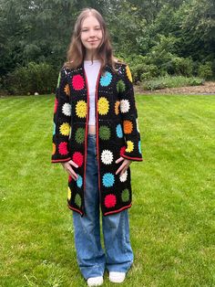 a woman standing in the grass wearing a black crocheted granny's sweater