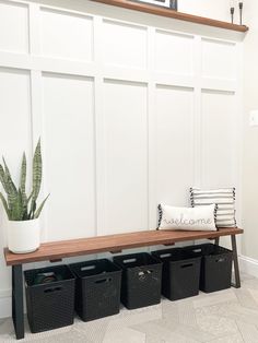 a wooden bench sitting next to a white wall with black baskets on top of it