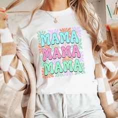 a woman in pajamas holding a drink and wearing a white shirt with the words mama on it