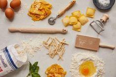 ingredients for pasta laid out on a white surface with flour, eggs and rolling pin