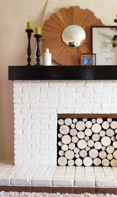 a fire place with logs stacked on top of it next to a mirror and candles