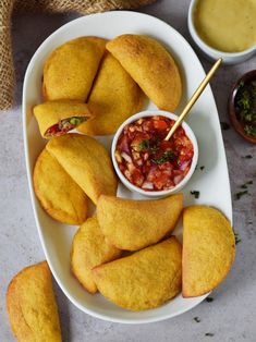 some food is on a white plate with dipping sauce in the middle and two small bowls next to it