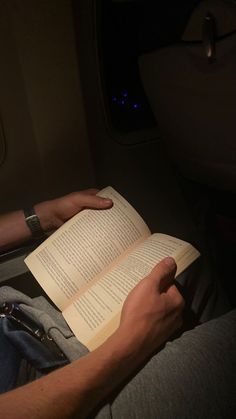 a man reading a book while sitting in an airplane with his feet on the seat