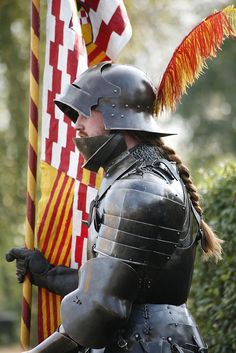 a man dressed in armor holding a flag and wearing a helmet with feathers on it