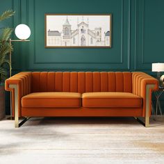 an orange couch sitting in front of a green wall next to a lamp and potted plant