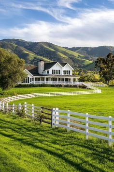 a large white house sitting on the side of a lush green field next to a white fence