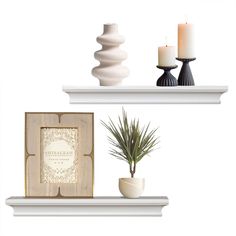 two white shelves with candles, a plant and a picture frame on top of them