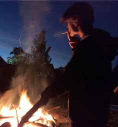 a man standing in front of a fire with his hand on the grill and looking at it