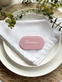 a place setting with white plates and pink napkins on top of each plate, along with greenery