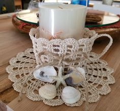 a candle and some seashells on a doily next to a glass cup