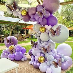 a bunch of balloons that are sitting on a table in the grass with butterflies flying over them