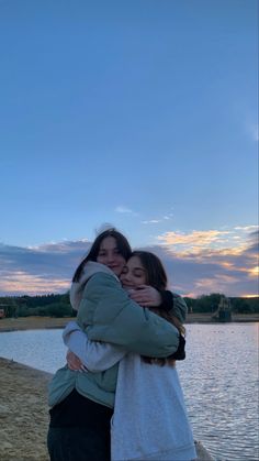 two women hugging each other by the water at sunset or dawn with clouds in the sky