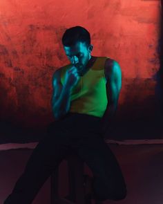 a man sitting on a stool in front of a red wall