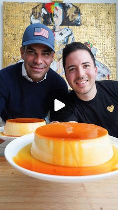 two men sitting in front of a cake on top of a white plate with orange sauce