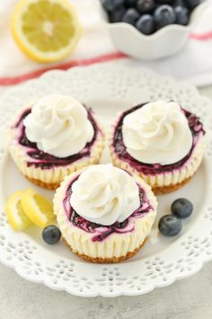 three blueberry cheesecakes on a white plate with lemon and blueberries in the background