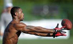 a shirtless man holding a football in his right hand and wearing gloves on the other