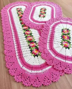 three crocheted placemats with pink and white flowers on them sitting on a wooden floor