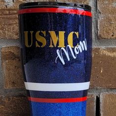 a blue and red coffee cup with the words usmc on it sitting next to a brick wall