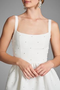 a woman in a white dress with pearls on her head and hands behind her back