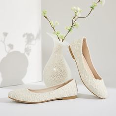 a pair of white shoes sitting next to a vase with flowers in it