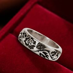 a silver ring sitting on top of a red velvet cushioned surface with black and white designs