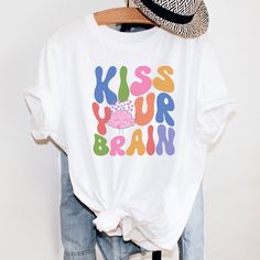 "Perfect gift for a Teacher or Special Education Teacher. I have said, \"Kiss your Brain,\" so many times in my classroom. This super cute retro teacher shirt makes a great teacher appreciation gift or a gift for a new graduating teacher. This is such a comfy, soft Tee with a loose fit, perfect to go with your favorite leggings. I use Bella+ Canvas t-shirts. UNISEX sizing they are meant to have a loose fit. Please refer to our sizing chart in the photos for measurements. *If you are looking for Fun Letter Print Shirt For Teacher Appreciation, Retro Crew Neck T-shirt For Teacher Appreciation, White Slogan T-shirt For School, White Slogan Shirt For School, Cute Multicolor Slogan T-shirt, Cute Multicolor T-shirt With Slogan, Fun T-shirt With Funny Print For Teacher Appreciation, Cotton T-shirt With Funny Print For Teacher Appreciation, Fun Cotton T-shirt With Letter Print